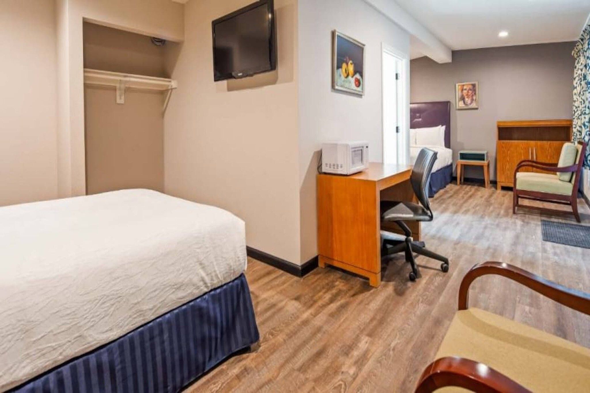 A hotel room with a bed, desk, chair, television, and artwork on the walls.