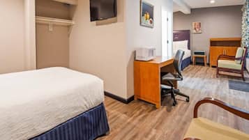 A hotel room with a bed, desk, chair, television, and artwork on the walls.