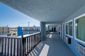 A corridor with a balcony on one side, leading to a building with multiple windows.