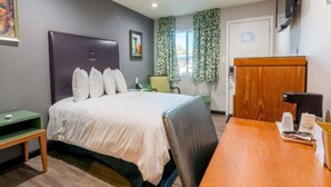 Ein Hotelzimmer mit einem Bett, einem Schreibtisch, einem Sessel, einem Fernseher und einem Fenster mit Vorhängen.