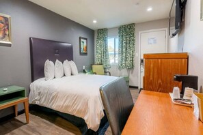 A hotel room with a bed, a desk, a chair, a television, and a window with curtains. - 1 King Bed | Non-Smoking, Micfridge (Ridgecrest CA)