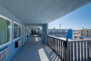 A long corridor with windows on one side and a balcony with a railing on the other.