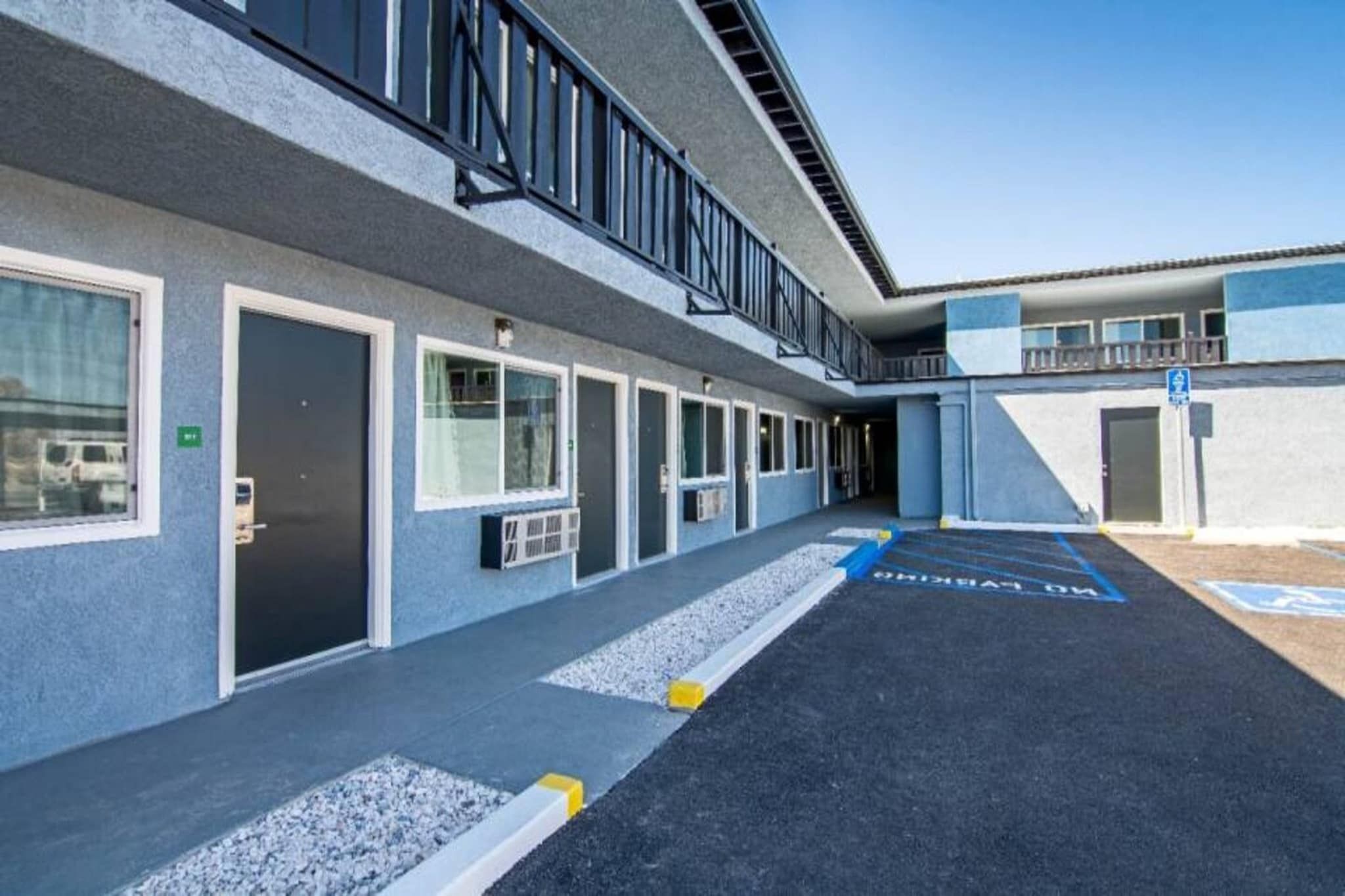 A building with a series of doors and windows, a parking area with handicapped parking spaces, and a clear sky.