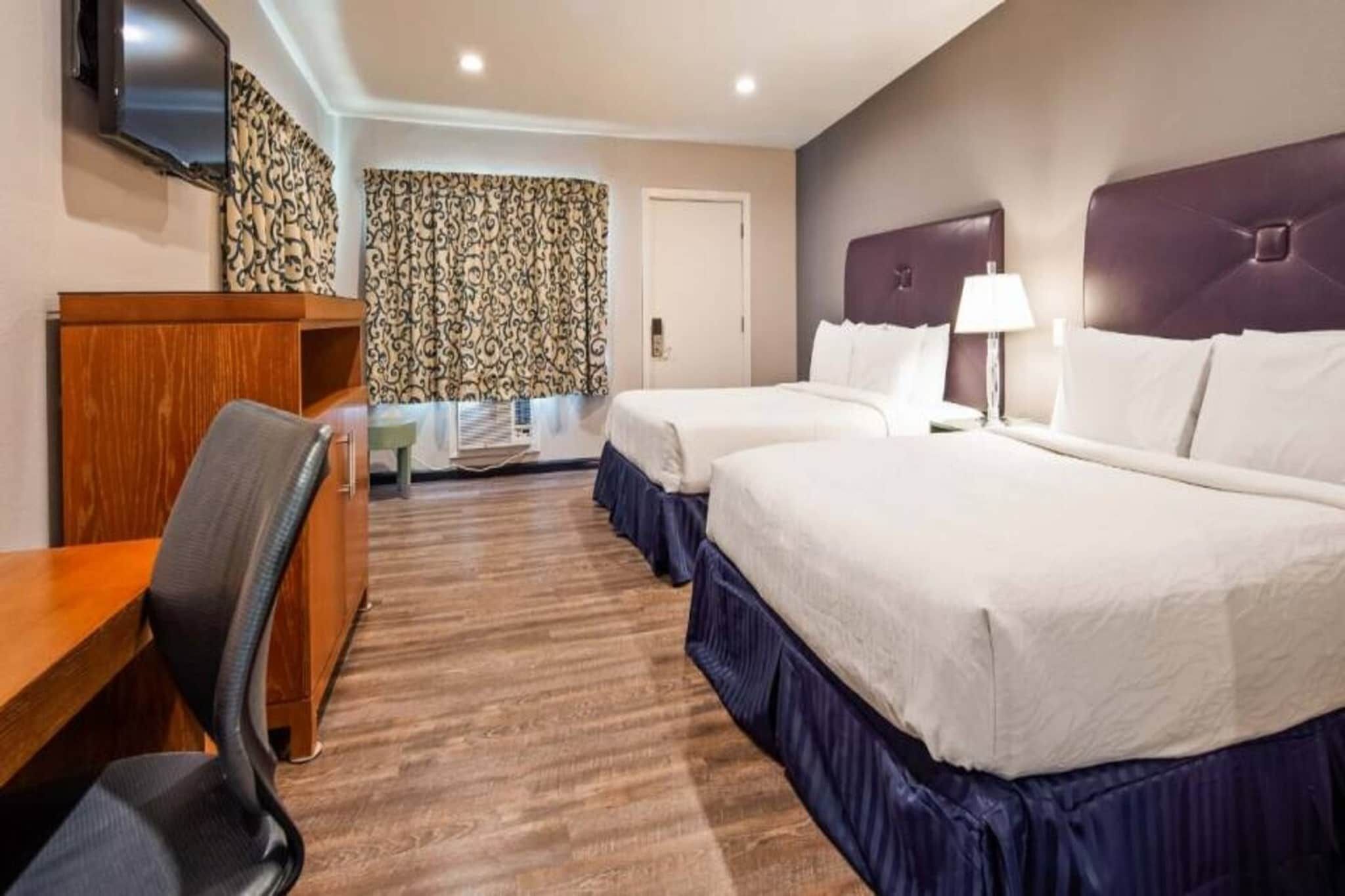 Habitación de hotel con dos camas, un escritorio, una silla, un televisor y una cortina estampada.