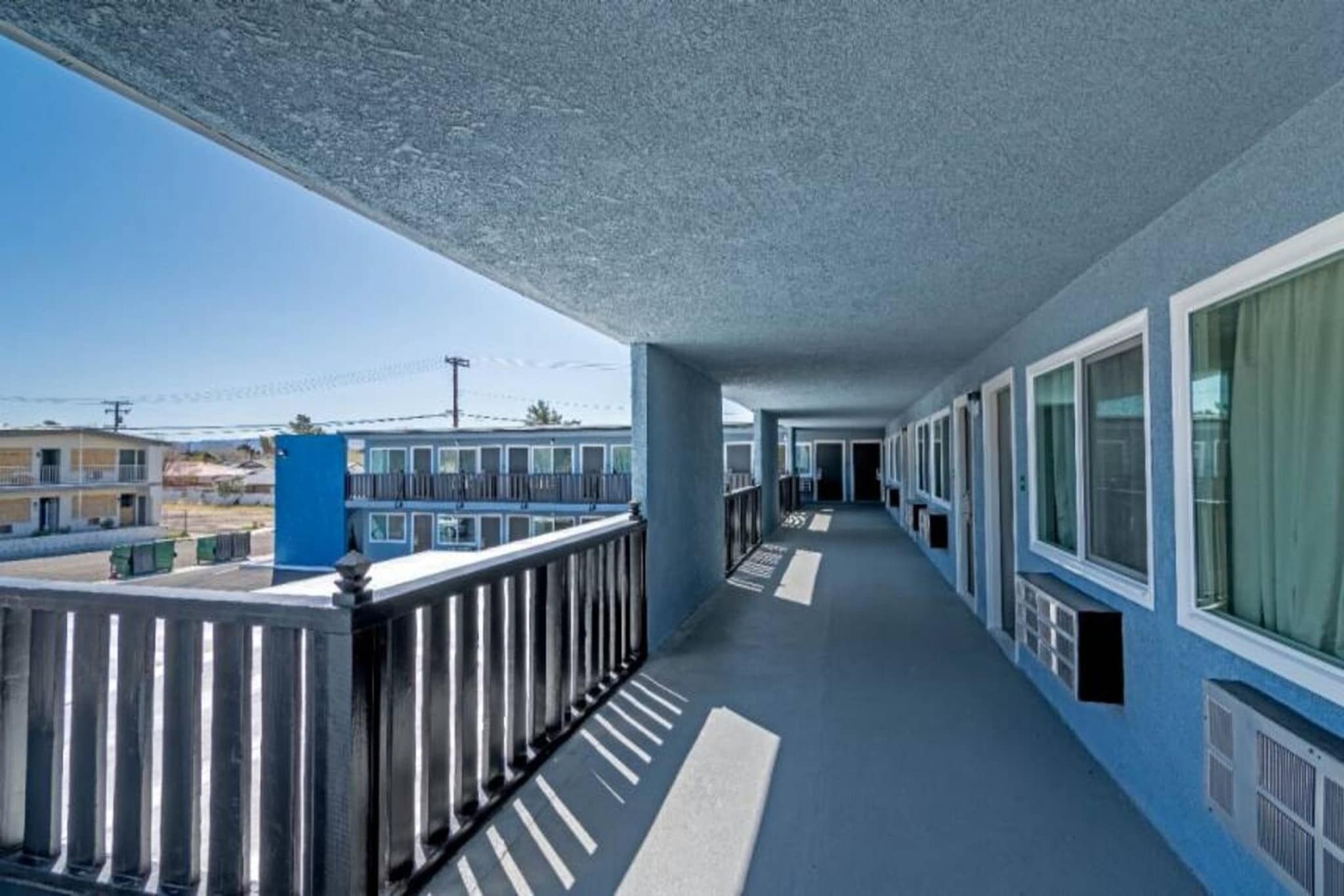 A corridor with a balcony on one side, featuring a metal railing and a blue exterior.