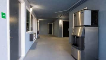 A hallway with a stainless steel refrigerator, a door with a green sign, and a window with blinds.