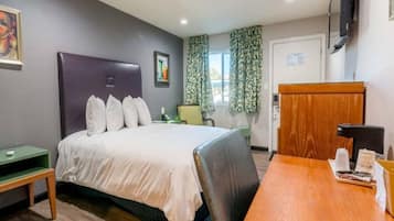 A hotel room with a bed, a desk, a chair, a television, and a window with curtains.