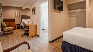 Ett hotellrum med en säng, ett skrivbord, en stol, en tv och en dörr som leder till ett annat rum.