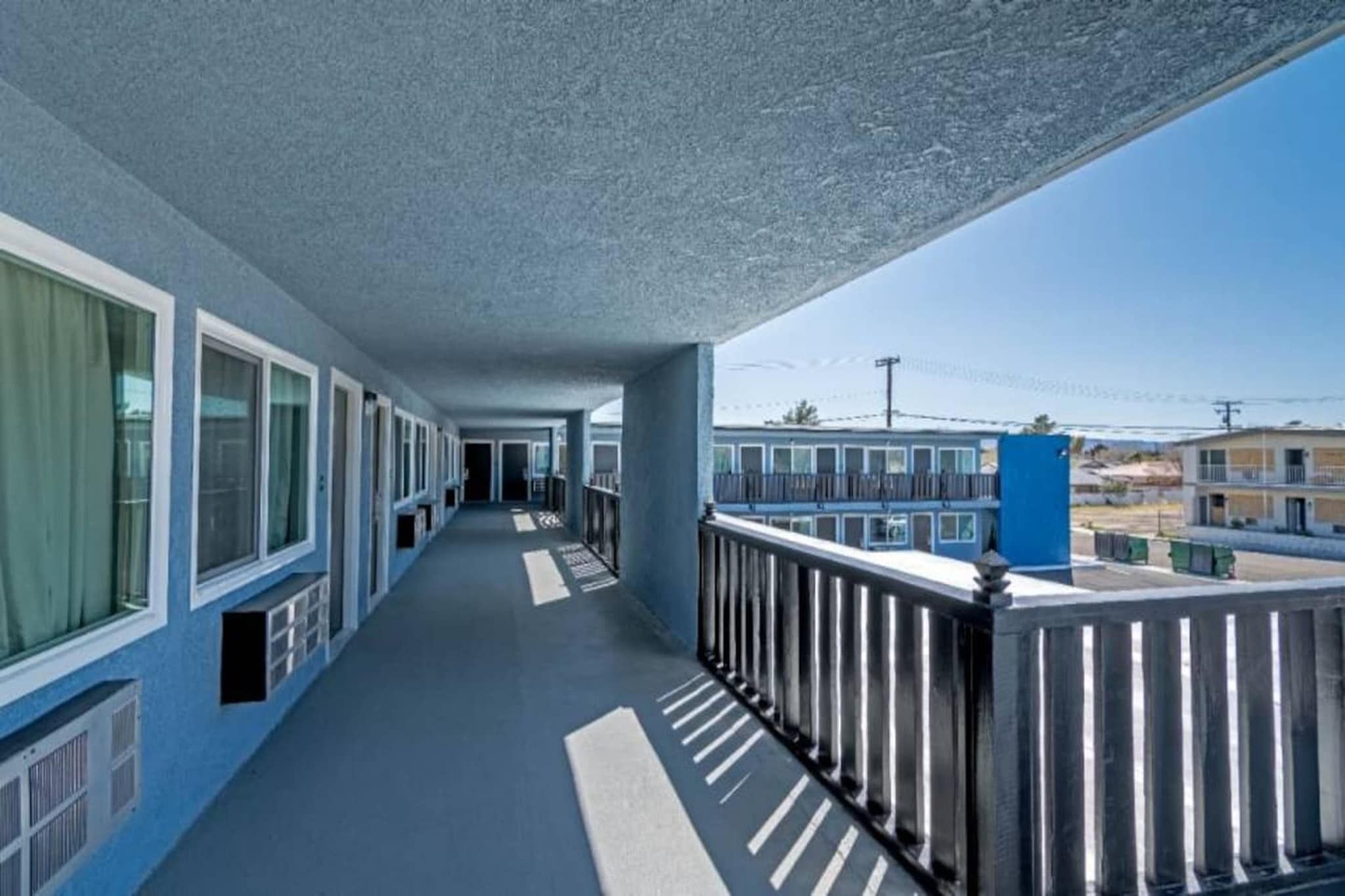 A long corridor with windows on one side and a balcony with a railing on the other.