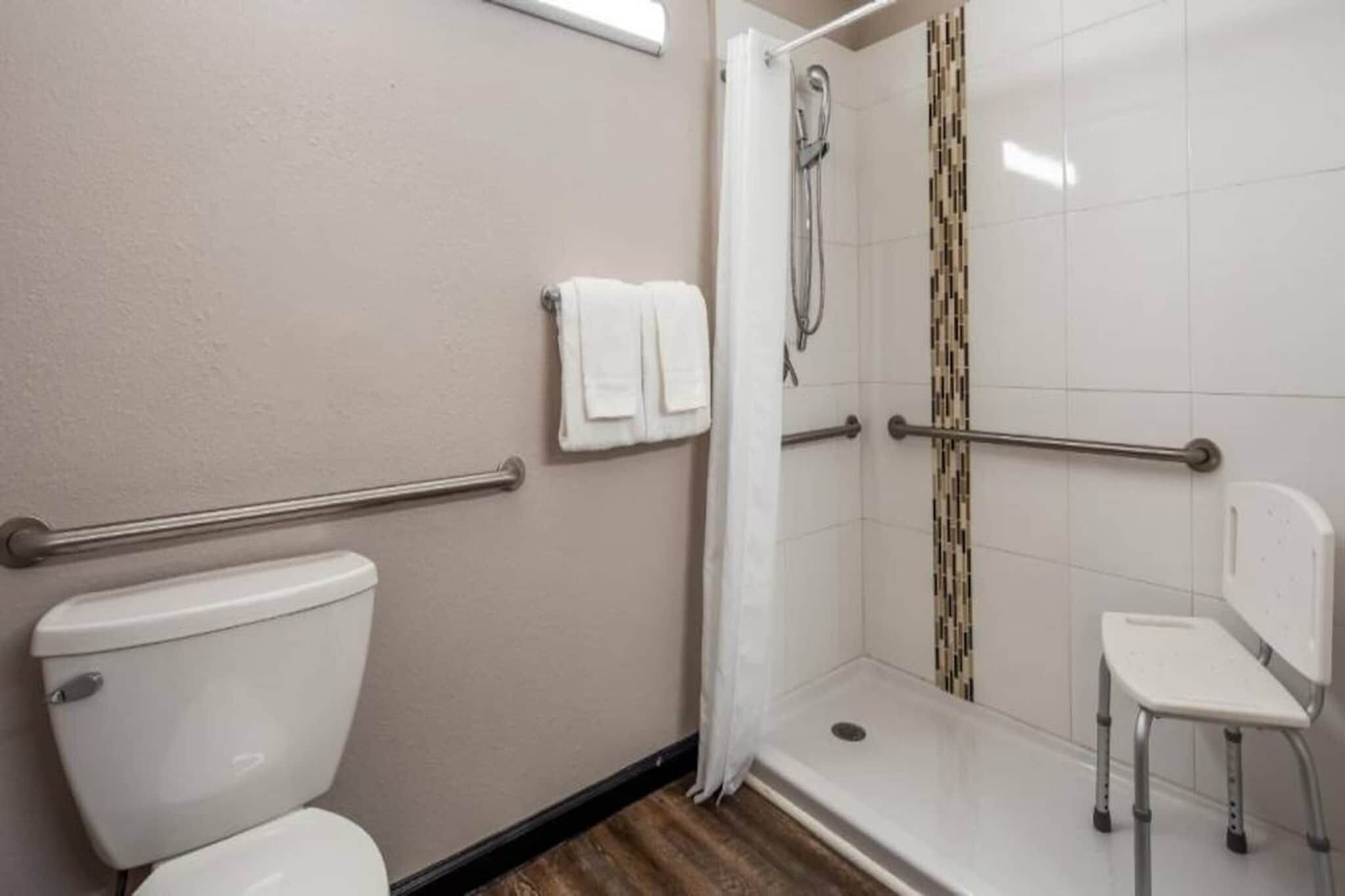 Ein Badezimmer mit Toilette, einer Dusche mit Haltegriff und einem Stuhl.