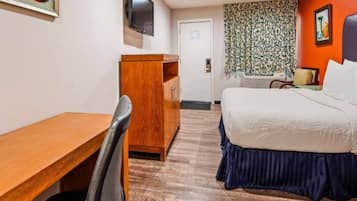 Quarto de hotel com escrivaninha de madeira, cama com cobre azul, televisão na parede e cortina estampada.
