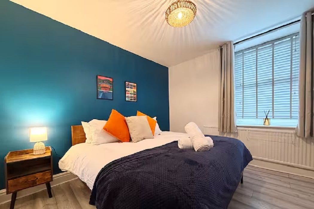 A bedroom with a bed, a nightstand, a lamp, and a window with blinds.