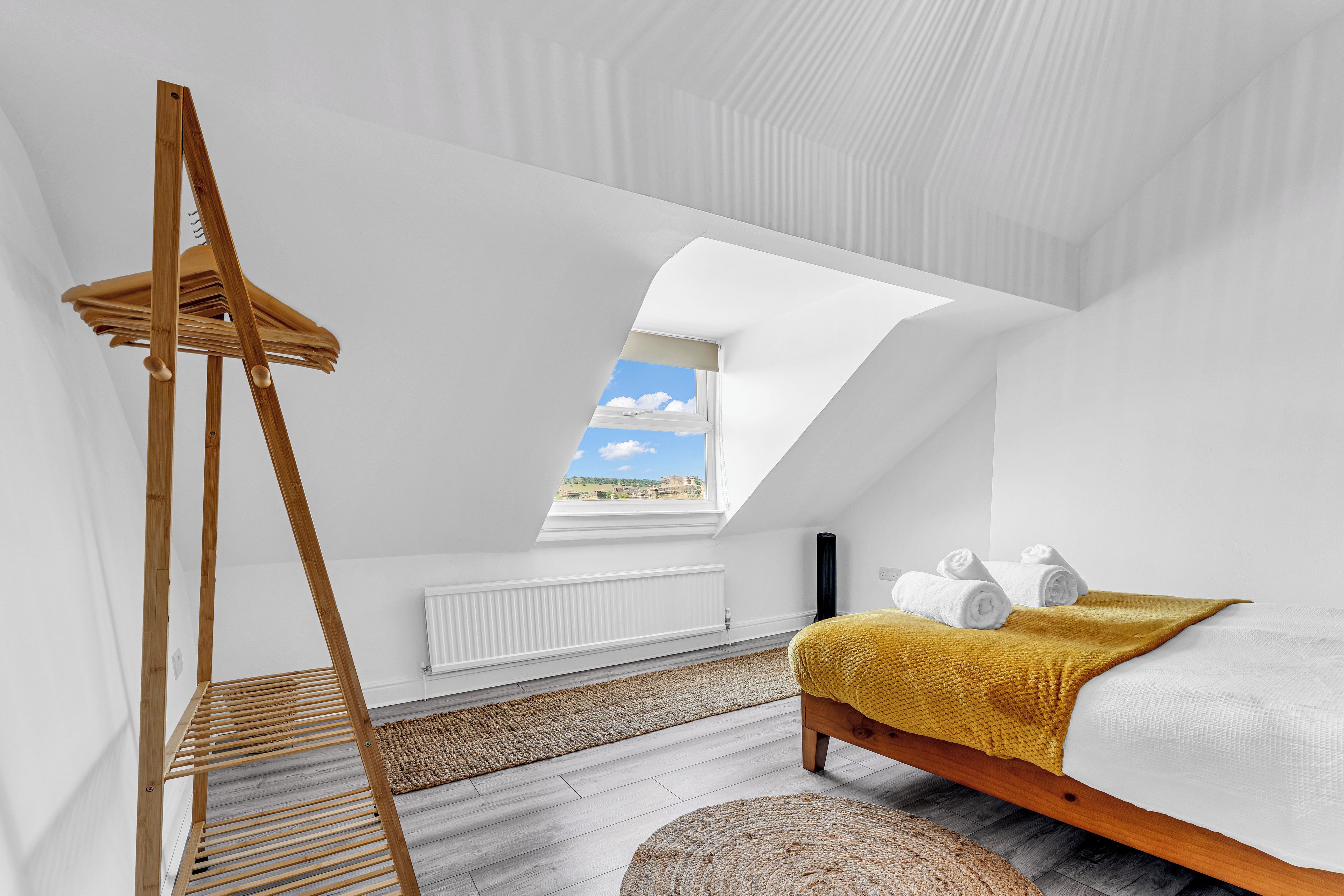 A bedroom with a skylight, a wooden ladder, a bed with a yellow blanket, and a view of the sky.