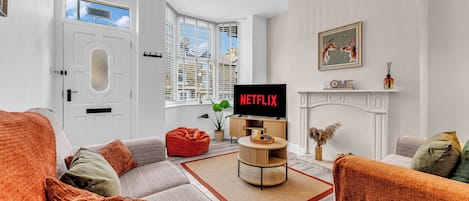 A living room with a sofa, a red bean bag, a coffee table, a fireplace, and a TV displaying 'NETFLIX'.