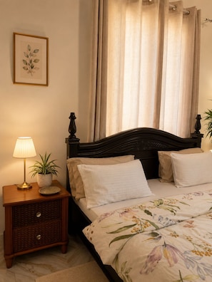 Une chambre à coucher avec un lit, une table de chevet avec une lampe et une plante, et un tableau encadré au mur.