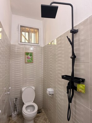 Une petite salle de bain avec des toilettes, une douche et une fenêtre.
