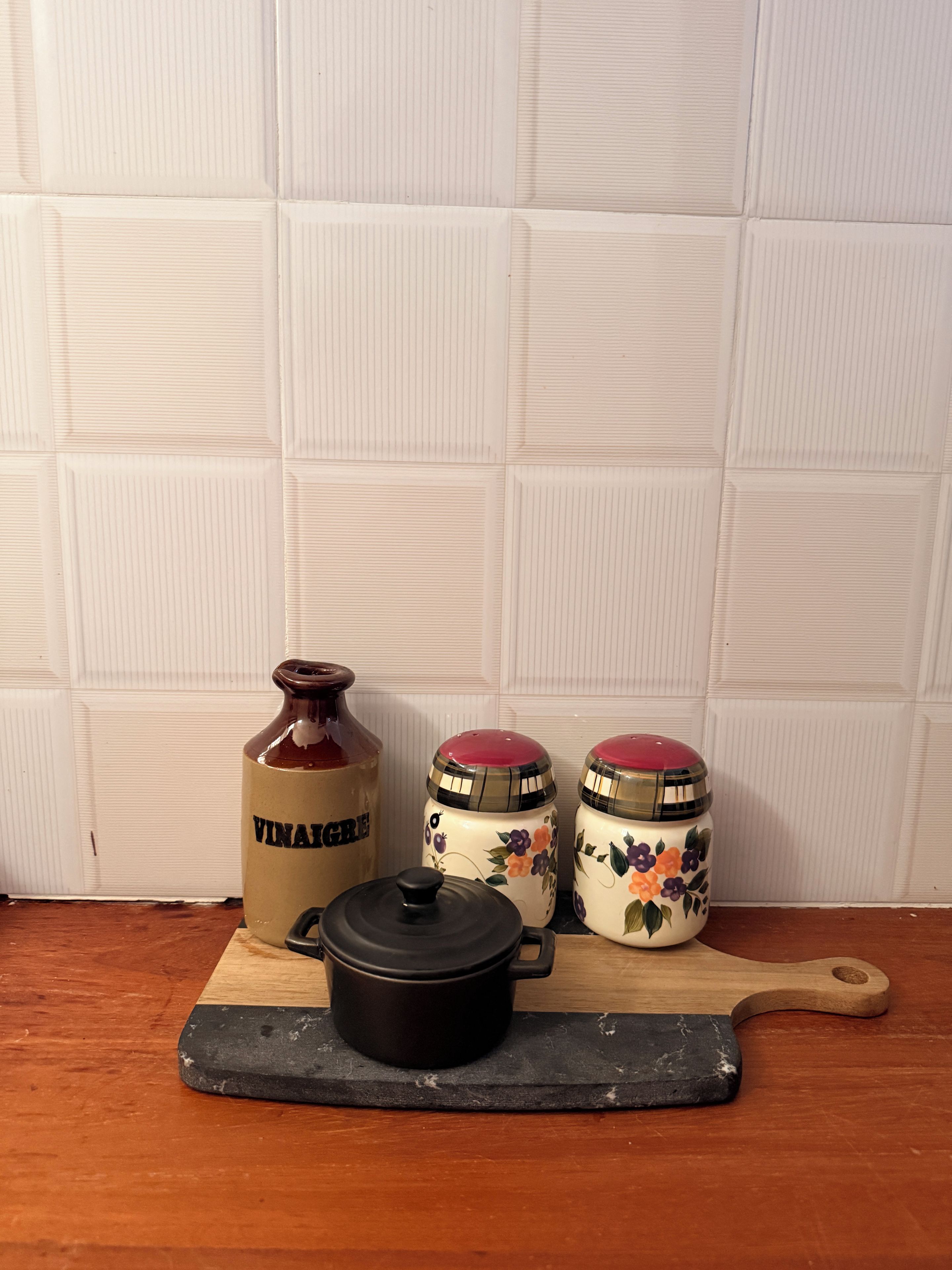 Una encimera de cocina con una tabla de cortar de madera, una olla negra y tres recipientes de cerámica con diseños florales.