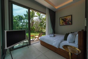 Ein Hotelzimmer mit einem großen Bett, einem Fernseher, einer Essecke mit Stühlen und Blick auf Grünflächen.