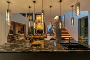 A modern kitchen with a marble countertop, pendant lighting, and a view of the living area. - Art-filled 6-bedroom villa, 12 m pool & walled garden – Layan, near Bang Tao (Tambon Choeng Thale)