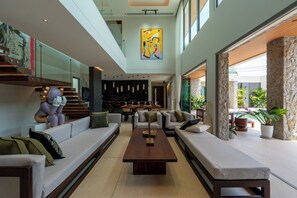 A spacious living area with a central coffee table, sofas, and a staircase leading to an upper level. - Art-filled 6-bedroom villa, 12 m pool & walled garden – Layan, near Bang Tao (Tambon Choeng Thale)
