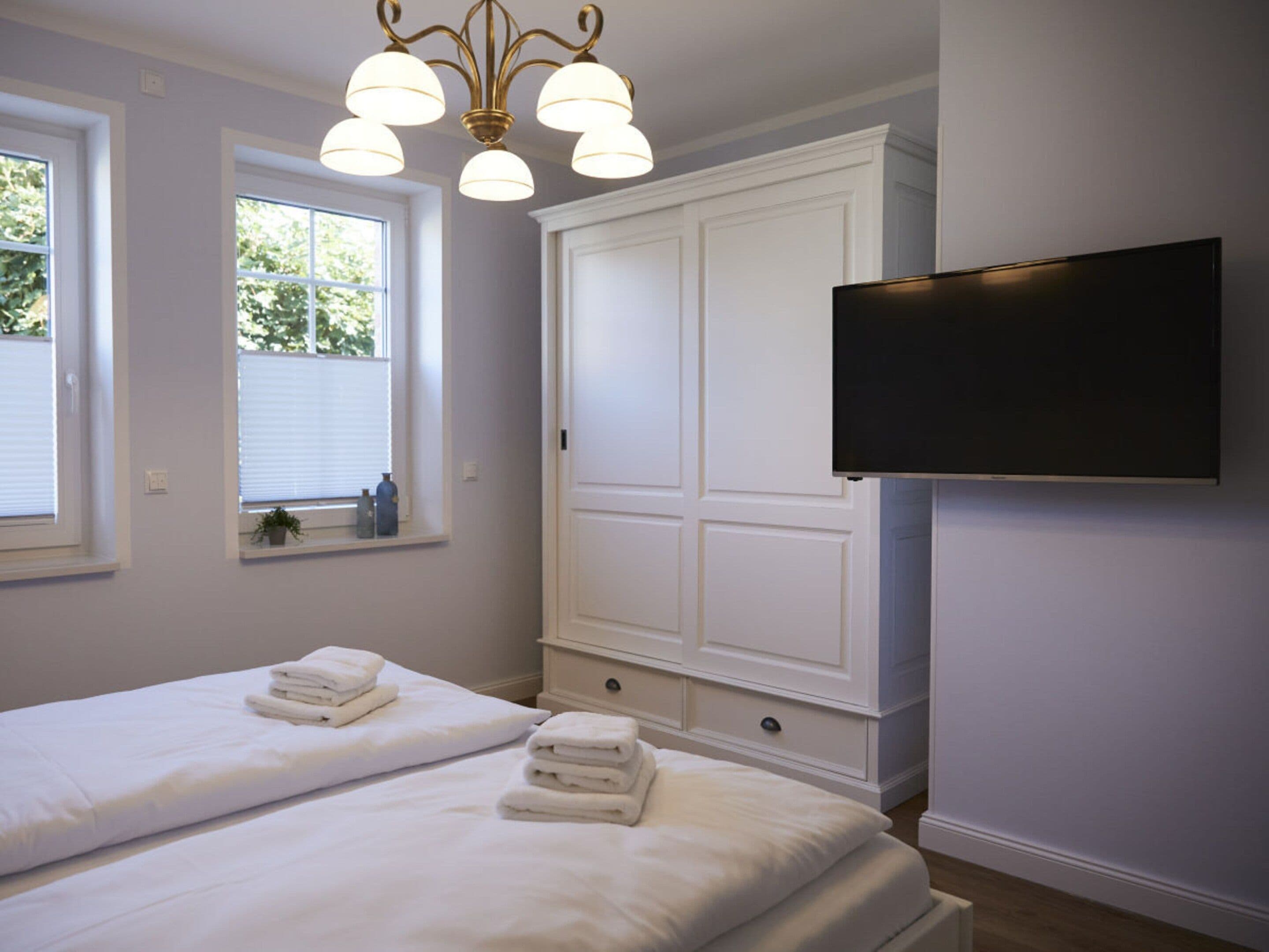 A hotel room with two beds, a TV mounted on the wall, and a window with blinds.