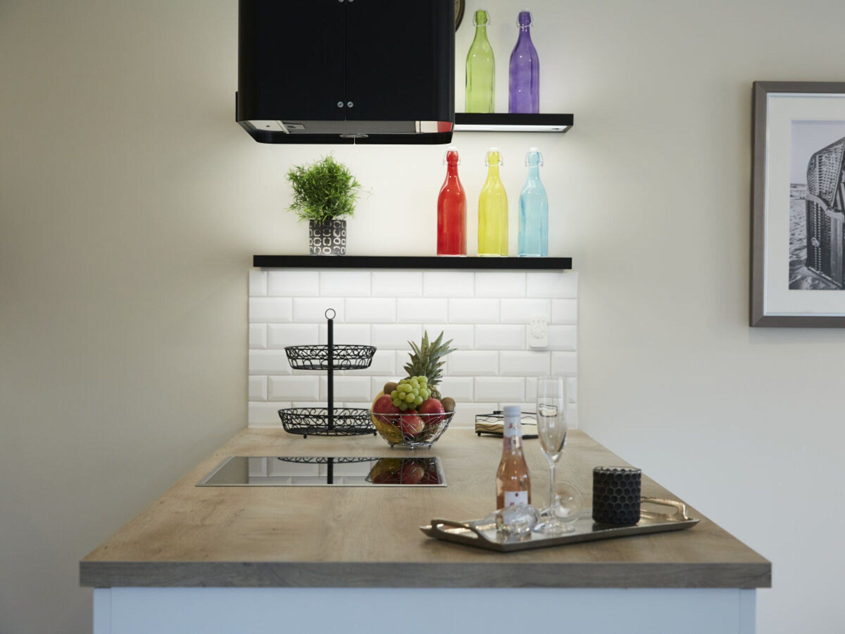 Une cuisine avec un plan de travail en bois, un panier de fruits, une bouteille de vin et un plateau avec des verres.