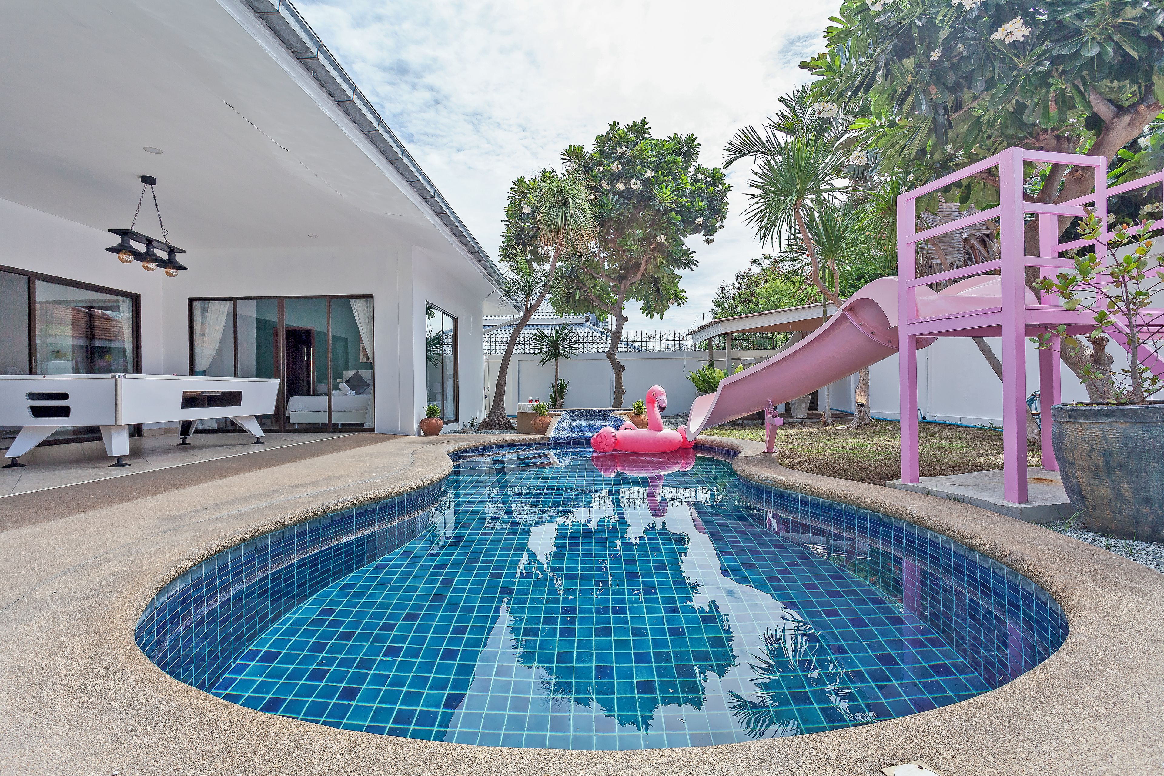 Une piscine avec un toboggan, un bâtiment blanc doté de grandes fenêtres et un arbre.
