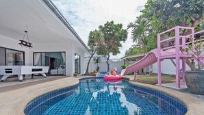 A swimming pool with a slide, a white building with large windows, and a tree. - 3-bedroom house in awesome Pattaya City with AC comfort (Pattaya City)