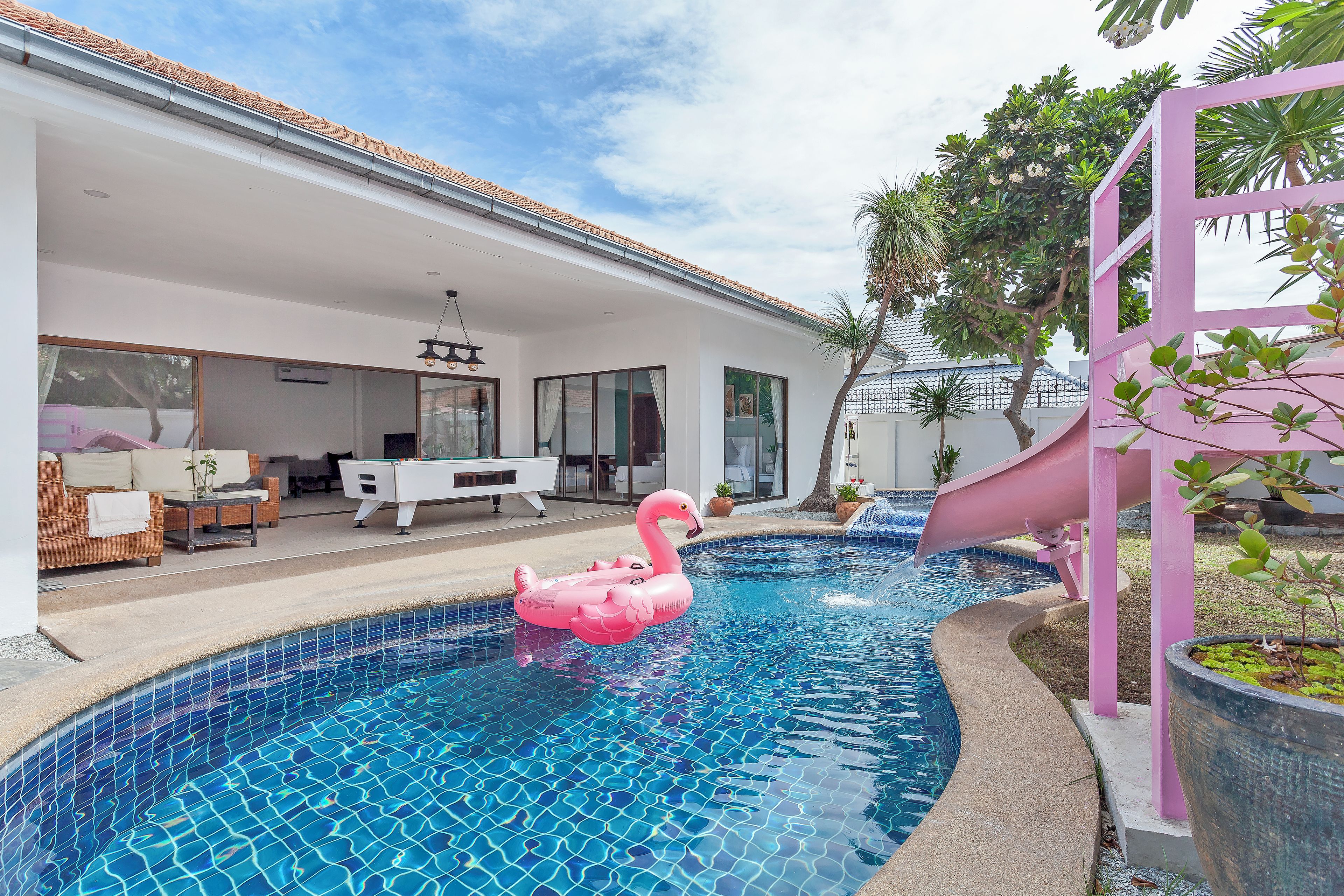 Ein Schwimmbecken mit einem rosa Flamingo-Schwimmding, einer Rutsche und einem überdachten Außenbereich mit Möbeln.