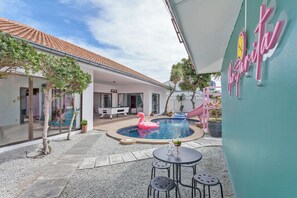 Un espace piscine agrémenté d’un flotteur en forme de flamant rose, d’une table de billard et d’un coin salon avec une table et des chaises.
