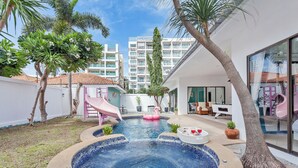 A swimming pool with a slide, surrounded by palm trees and a building with a tiled roof. - 3-bedroom house in awesome Pattaya City with AC comfort (Pattaya City)