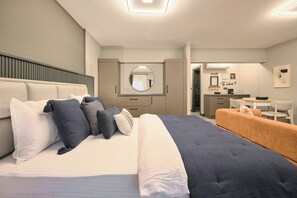 Ein modernes Schlafzimmer mit einem großen Bett, Nachttischen, einem Spiegel und einer kleinen Küchenzeile.