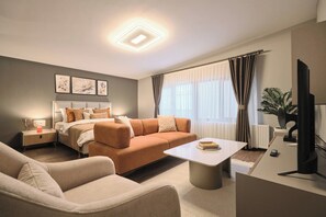 Ein modernes Wohnzimmer mit Sofa, Couchtisch, Fernseher und einem Bett mit Kopfteil.