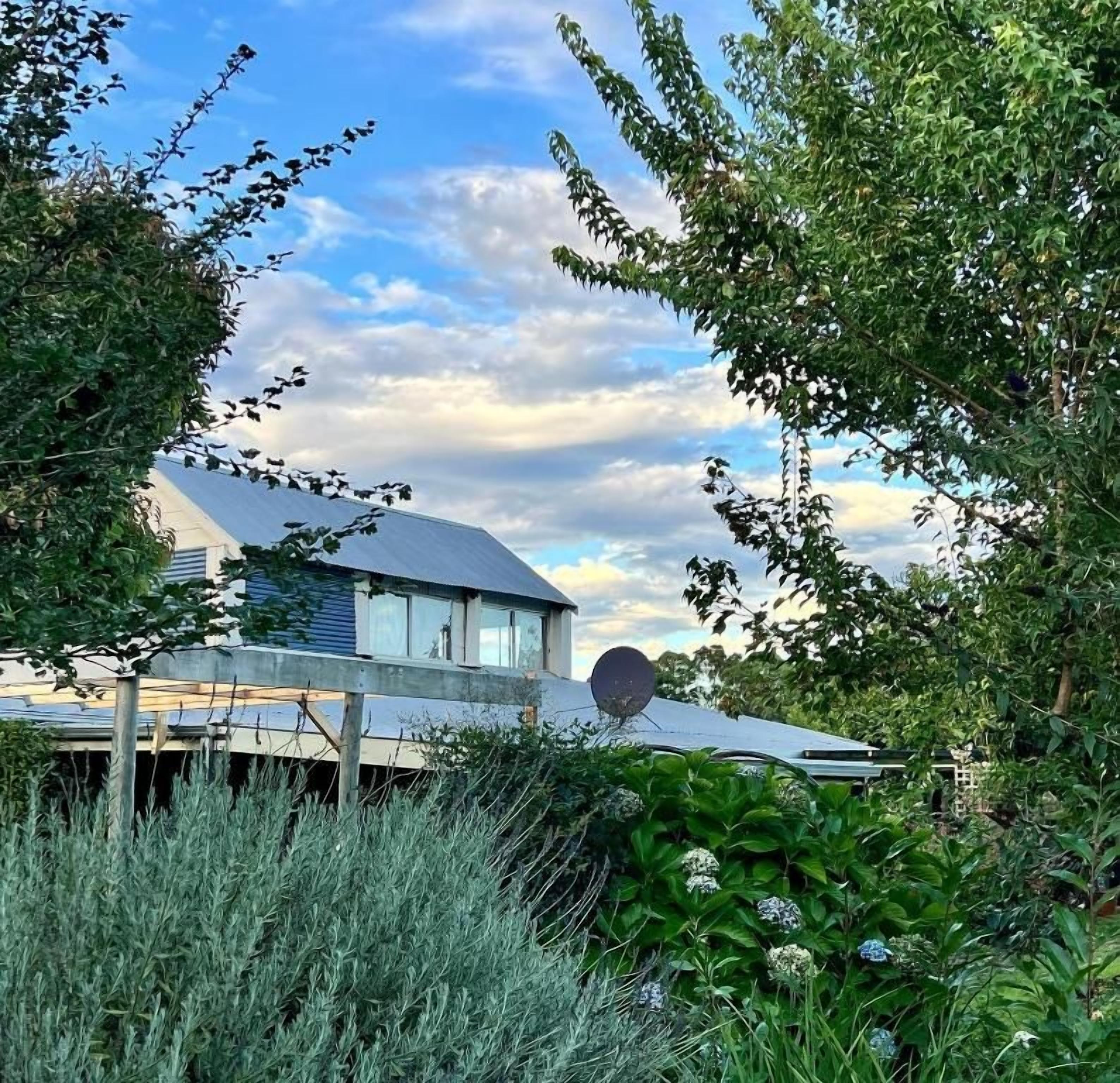 A house with a satellite dish, surrounded by lush greenery and a clear sky.