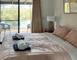 A hotel room with a bed, a nightstand, a lamp, and a view of the outdoors.