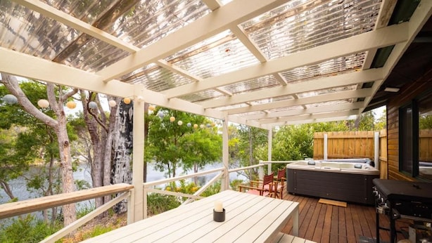 Una terraza al aire libre con una mesa de madera, un jacuzzi y una parrilla.