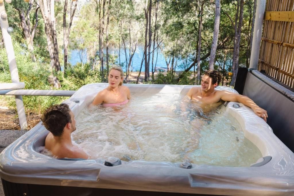 A hot tub with three people, surrounded by trees and a bamboo fence.