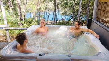 A hot tub with three people, surrounded by trees and a bamboo fence.