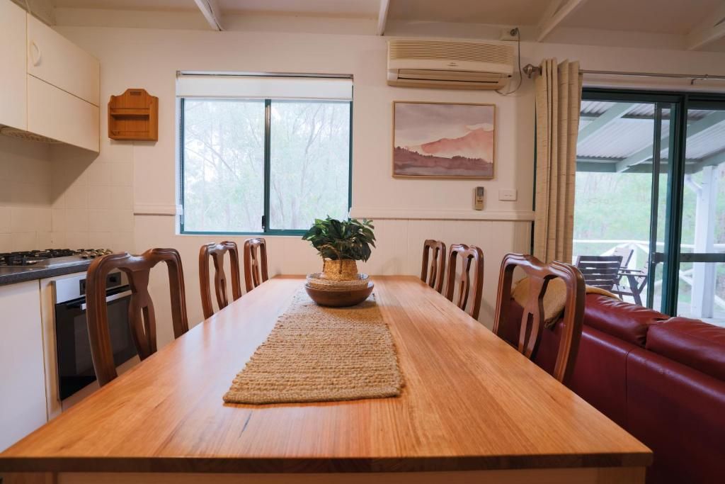 Un comedor con una mesa de madera, sillas, una planta en maceta y un sofá de cuero rojo.