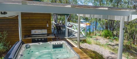 Una cabaña de madera con jacuzzi, mobiliario exterior y una terraza con vistas a un cuerpo de agua.