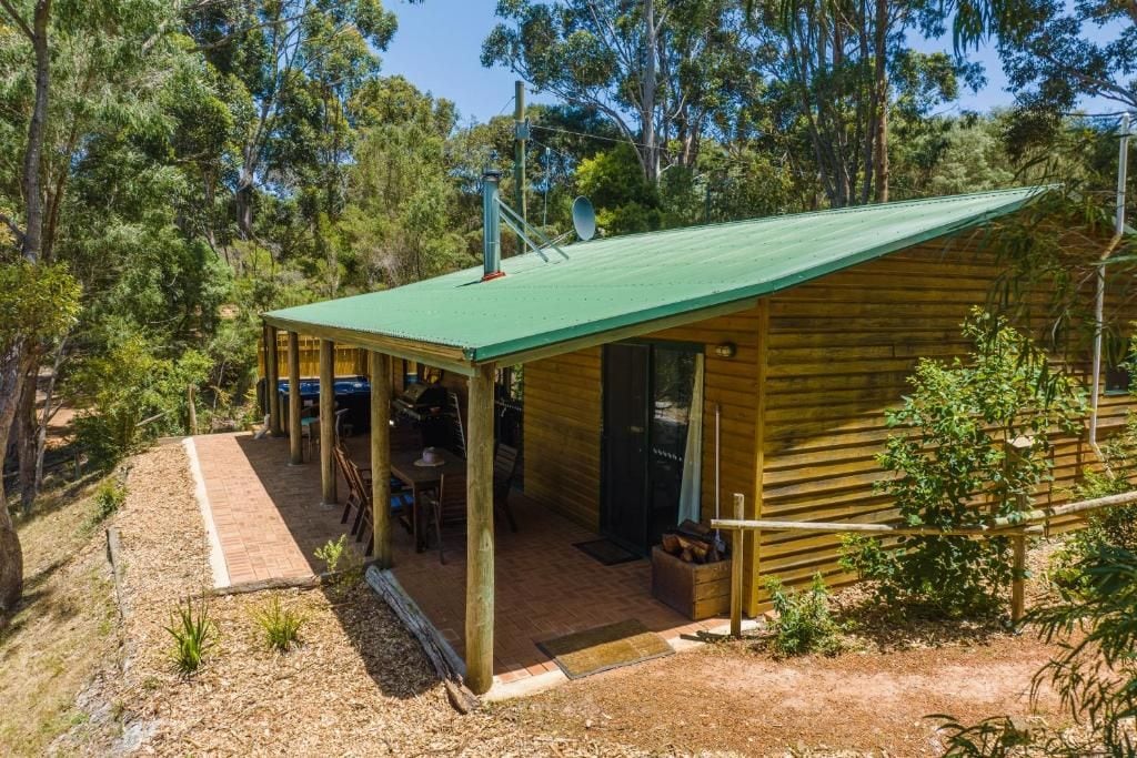 A wooden cabin with a green roof, surrounded by trees.