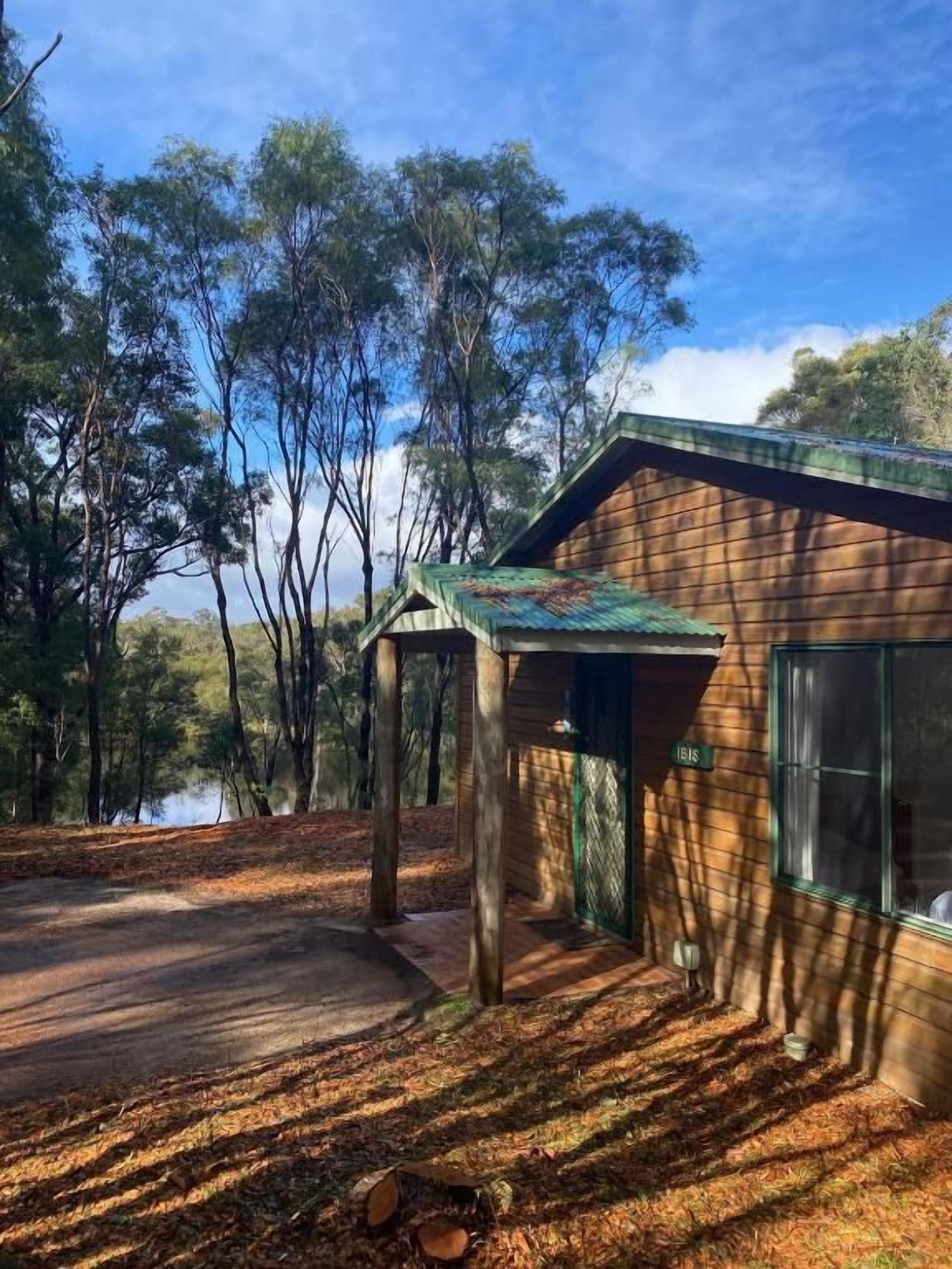 Un edificio de madera con techo verde, rodeado de árboles y una masa de agua.