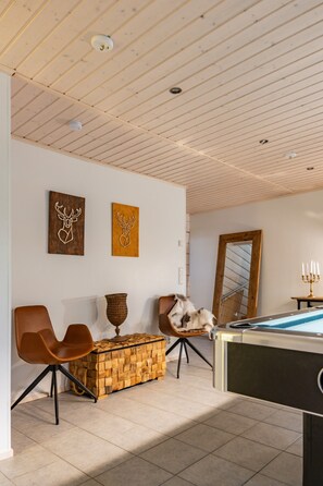 A room with a pool table, two chairs, a woven chest of drawers, and wall art. - Villa Hutiputti A · Pool · Ski & Golf (Kittilä)