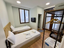 A hotel room with two single beds, a TV mounted on the wall, a wooden bunk bed, and a clothing rack.