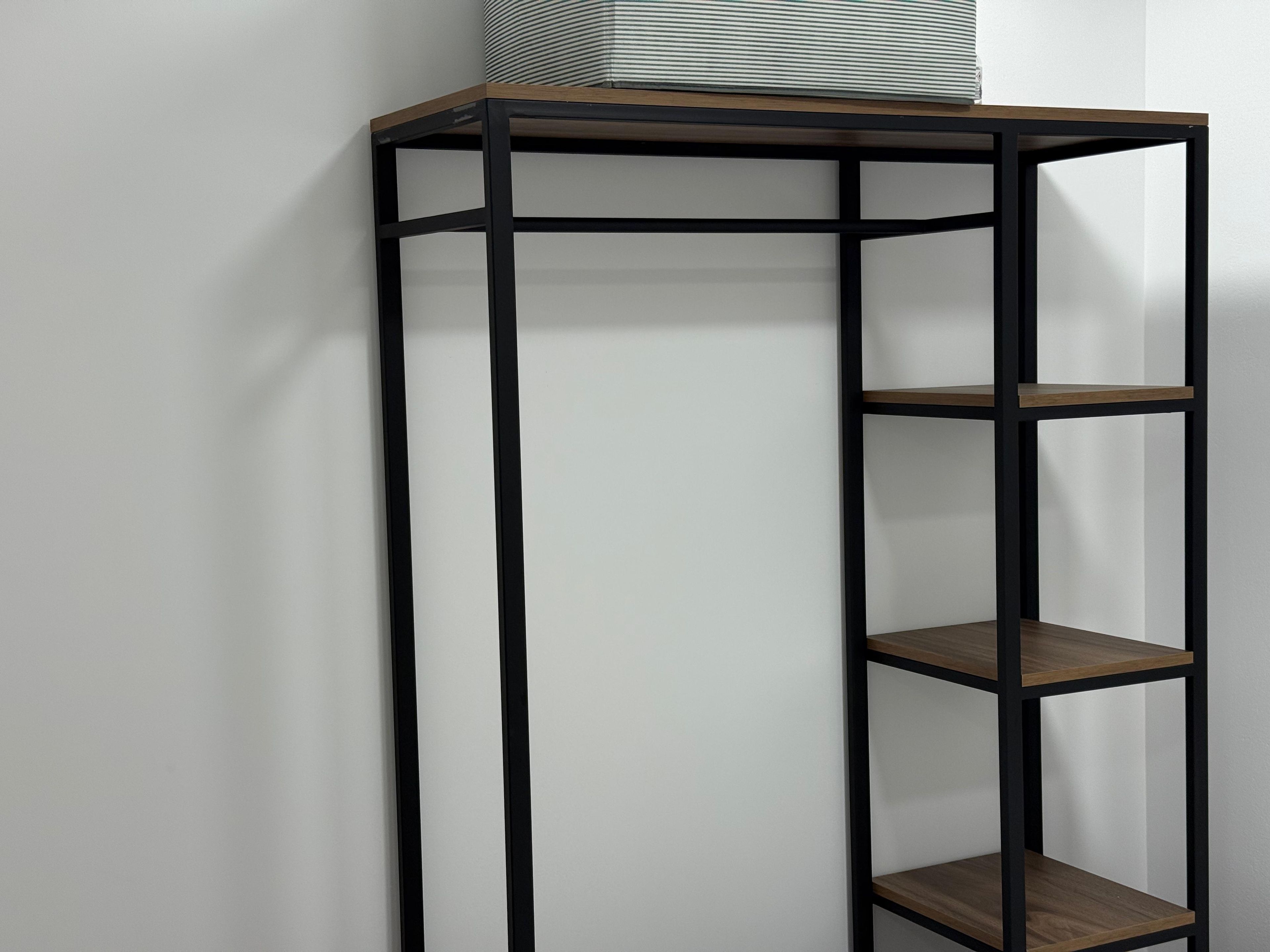 Een hoge, smalle metalen plankenwand met drie planken, geplaatst tegen een effen muur.