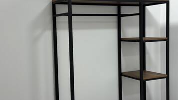 Een hoge, smalle metalen plankenwand met drie planken, geplaatst tegen een effen muur.