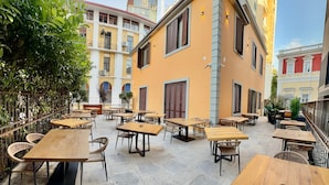 An outdoor cafe with multiple wooden tables and chairs, surrounded by a metal fence and greenery. - Rali Hotel & Restaurant (Tiranë)