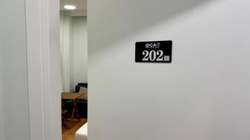 A hallway with a door labeled 'DCA 202' and a glimpse of a room with a bed and a desk.