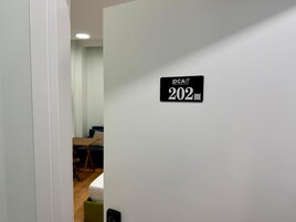 A hallway with a door labeled 'DCA 202' and a glimpse of a room with a bed and a desk.