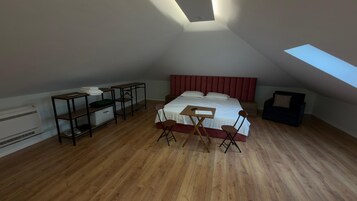Un dormitorio con techo inclinado, una cama, un escritorio, una silla, una mesita y un sofá.